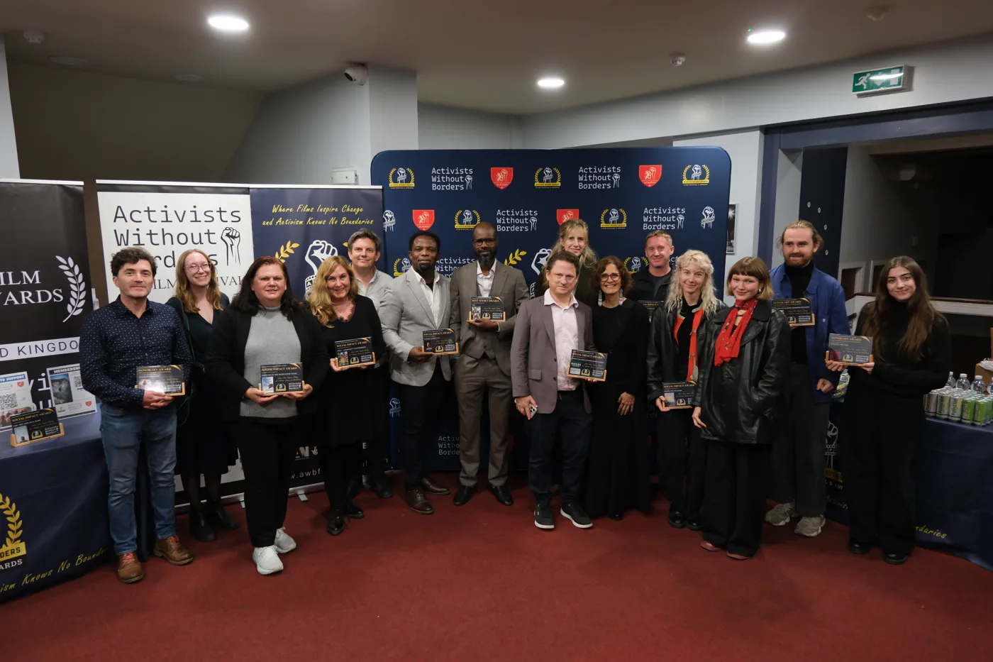 About twenty people standing in rows holding award plaques in front of an Activists Without Borders backdrop