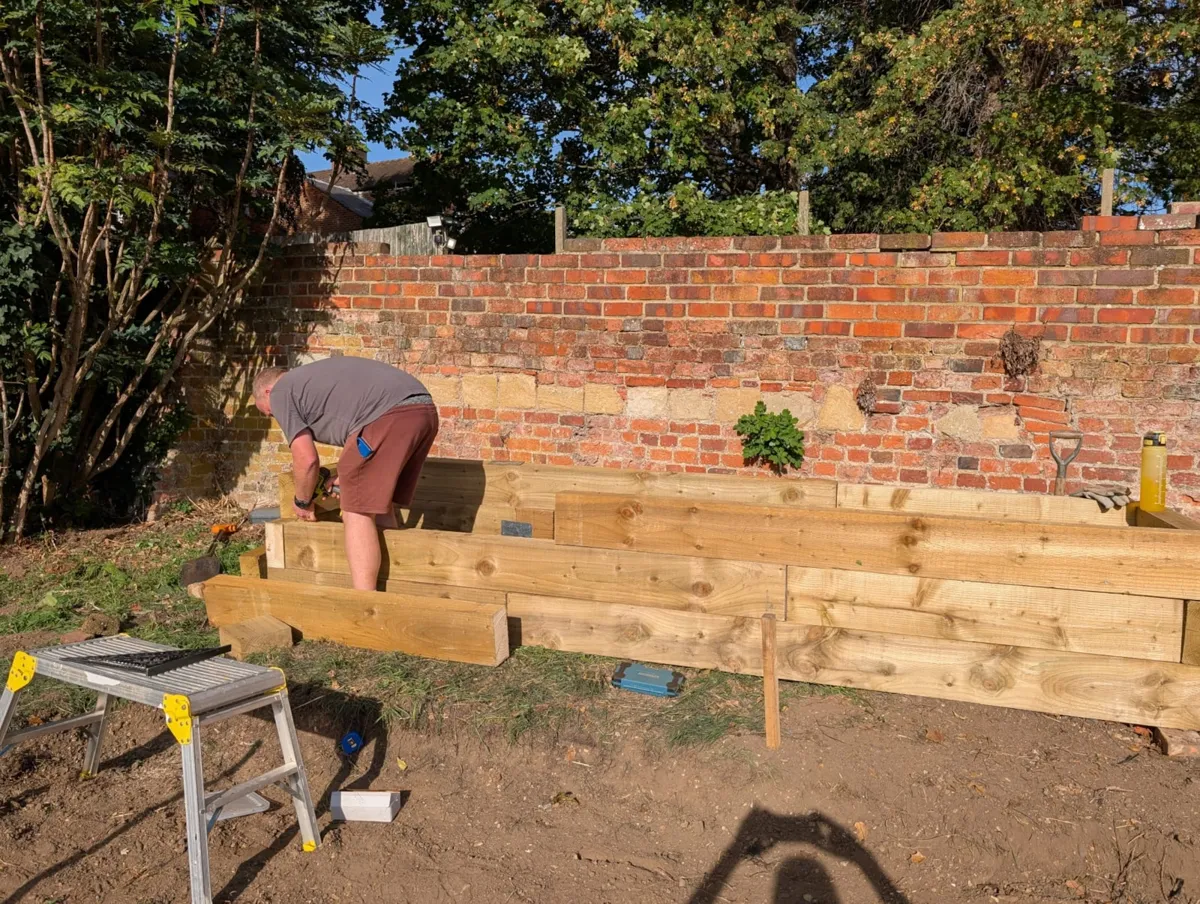 A volunteer assembling timber raised beds against an old brick wall on the garden plot next to Reading Civic Centre